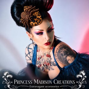 May include: A leopard print fascinator featuring a beaded spider ornament in bronze tones. The accessory is worn in a high hairstyle. Text at the bottom reads: PRINCESS MADISON CREATIONS, Extravagant accessories, www.etsy.com/shop/princessmadcreations.