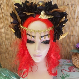 May include: A black and gold floral crown with a skull accent. The crown is adorned with black flowers, gold leaves, and a gold chain with tassels.