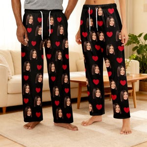 Könnte beinhalten: Schwarze Schlafanzughose mit einem sich wiederholenden Muster aus roten Herzen und einem Gesicht. Die Hose hat einen Kordelzug in der Taille. Diese bequeme Schlafanzughose ist für Entspannung und Freizeit konzipiert.