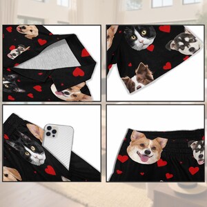 K&ouml;nnte beinhalten: Schwarzes Pyjama-Set mit einem Muster aus Hunde- und Katzenk&ouml;pfen und roten Herzen. Das Set besteht aus einem lang&auml;rmligen Oberteil und Shorts. Ein wei&szlig;es Smartphone befindet sich in der Hosentasche.