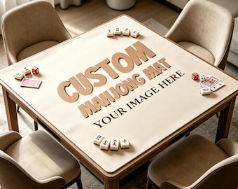 May include: A square beige mahjong mat placed on a wooden table, featuring the text CUSTOM MAHJONG MAT YOUR IMAGE HERE in large brown letters. The mat is surrounded by four beige chairs and includes scattered mahjong tiles, dice, and playing cards.
