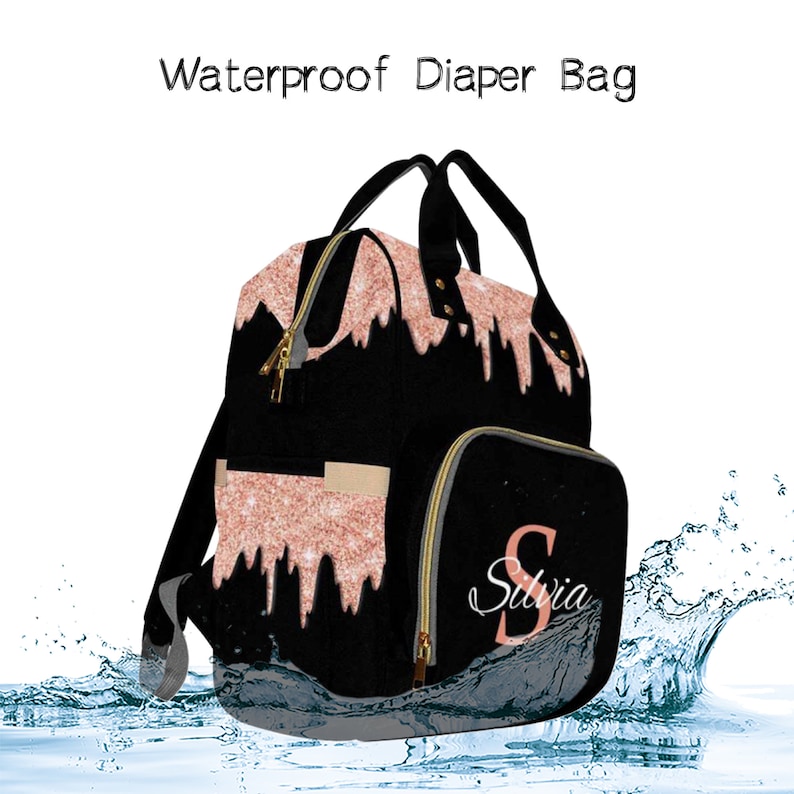 May include: Black diaper bag with a rose gold glitter design and the name "Silvia" on the front. The bag is waterproof and has a zipper closure. It is shown in a water splash.