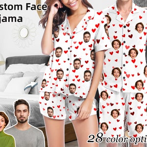 Może przedstawiać: Para w dopasowanych białych piżamach z czerwonymi sercami i nadrukowanymi twarzami. Na zdjęciu widoczny jest tekst "Custom Face Pajama" i "28 opcji kolorystycznych".