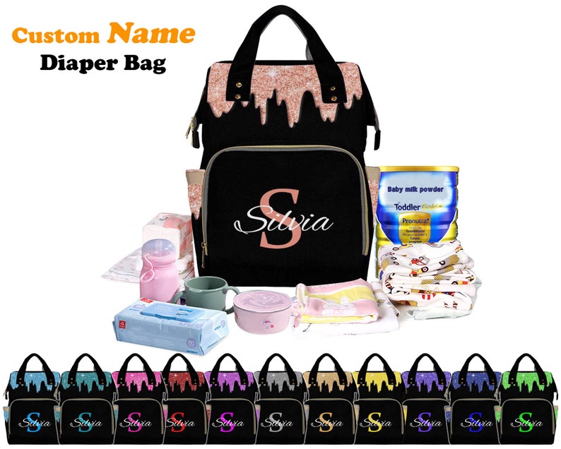 May include: A black diaper bag with a pink glitter design and a pink "S" monogram. The bag is shown with various baby items, including a bottle of baby formula, a container of baby wipes, a sippy cup, and a baby blanket.