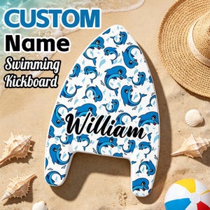 May include: A white swimming kickboard featuring a repeating pattern of blue dolphins and the name William printed in black script across the center. The board has a pointed top and two bottom handles, designed for use in water activities.