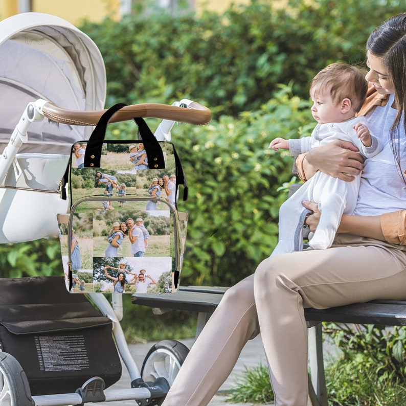 May include: A black and beige diaper bag with a collage of family photos printed on the front. The bag is hanging on a stroller.