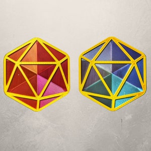 May include: Two gold-rimmed, iridescent, geometric dice with a 12-sided shape. The dice are made of a translucent material, with one die showing shades of red and pink, and the other showing shades of blue and green.