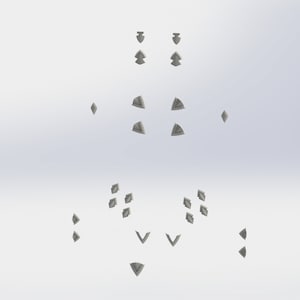 May include: A collection of silver-colored metal studs in various shapes, including triangles, squares, and diamonds. The studs are arranged in a symmetrical pattern on a white background.