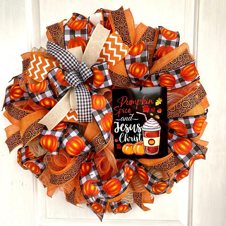 Pu&ograve; includere: Una ghirlanda autunnale con nastro a quadri arancio, nero e bianco, rete arancione e un cartello che recita "Pumpkin Spice and Jesus Christ".