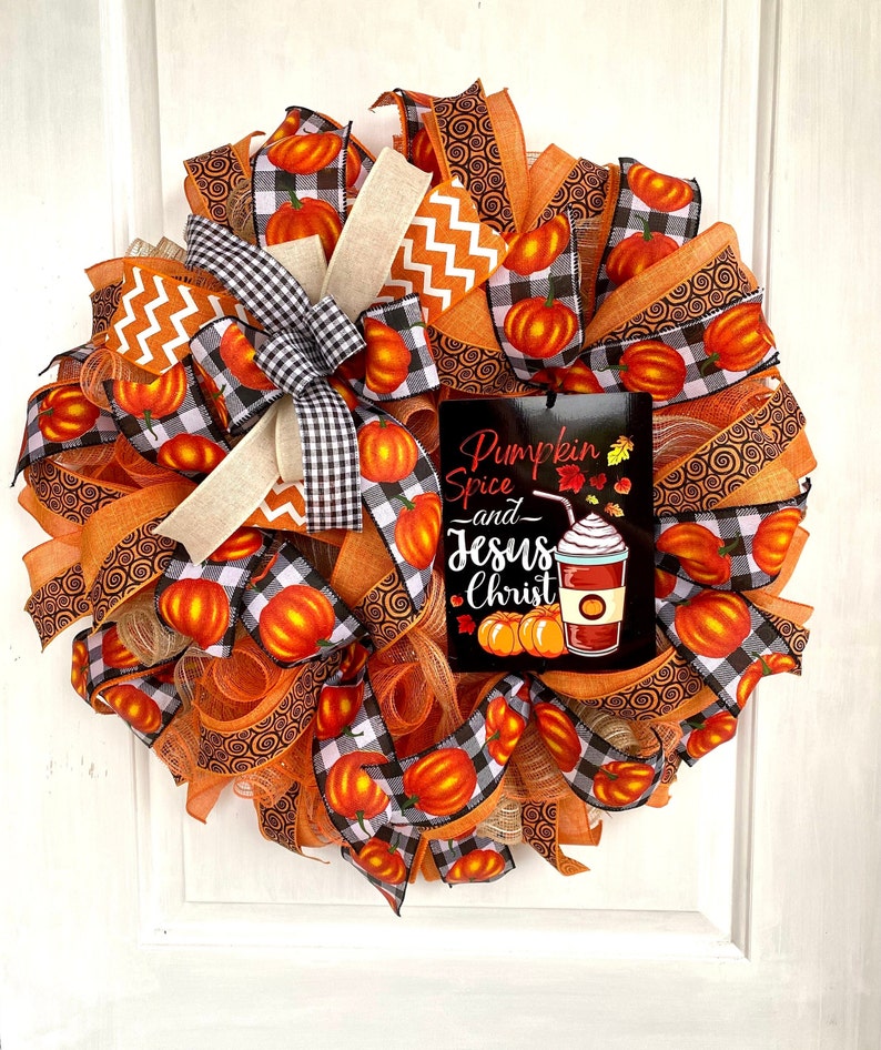 Pu&ograve; includere: Una ghirlanda autunnale con nastro a quadri arancio, nero e bianco, nastro a spirale arancio e marrone e un cartello con la scritta "Pumpkin Spice and Jesus Christ".