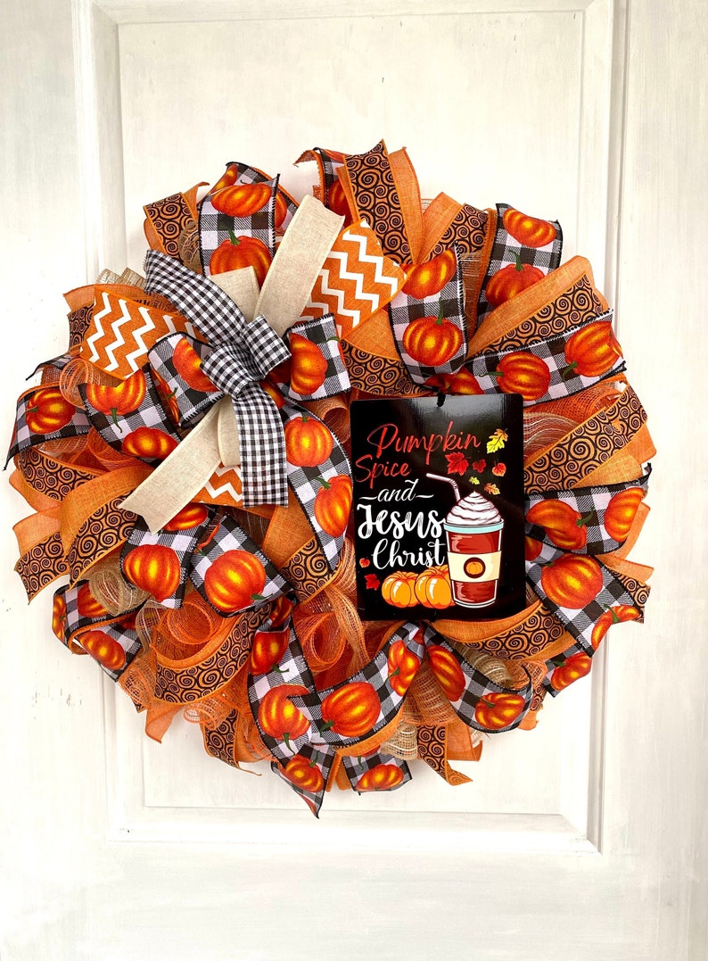 Pu&ograve; includere: Una ghirlanda autunnale con nastro a quadri arancio e nero, nastro arancio con motivo a spirale e un cartello che recita "Pumpkin Spice and Jesus Christ".