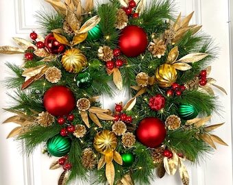 May include: A festive Christmas wreath with green pine needles, red and gold ornaments, gold leaves, and small pinecones. The wreath is decorated with red berries and small lights, creating a warm, inviting holiday decoration.