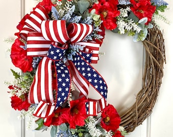 Könnte beinhalten: Eine patriotische Kranz mit leuchtend roten Mohnblumen, weißen und blauen Akzenten und einer großen Schleife mit Streifen und Sternen der amerikanischen Flagge. Der Kranz besteht aus geflochtenen Zweigen.