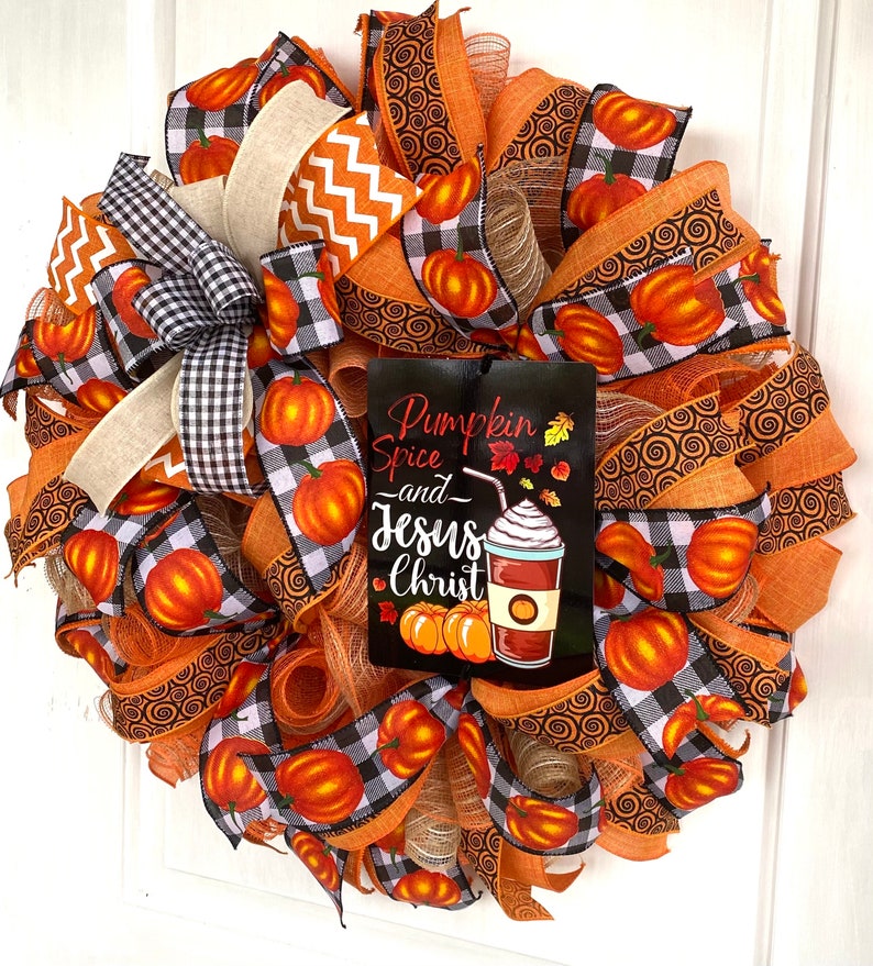 Pu&ograve; includere: Una ghirlanda autunnale con nastro a quadri arancio e nero, nastro arancio con motivo a spirale e un cartello che recita "Pumpkin Spice and Jesus Christ".