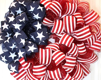 May include: A red, white, and blue patriotic wreath made with mesh and ribbon. The wreath is decorated with red and white striped ribbon and blue ribbon with white stars.