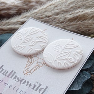 May include: A pair of white ceramic earrings with a leaf design. The earrings are round and have a raised design. The earrings are on a white card with the text "halbsowild jewellery etsy.com/shop/halb"