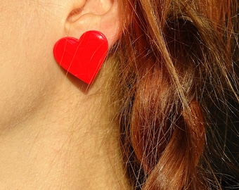 May include: A close-up of a person's ear with a red heart-shaped earring. The person has long, red hair.