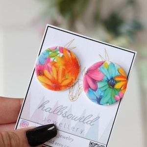 Puede incluir: Un par de pendientes redondos y florales de colores. Los pendientes están hechos de arcilla polimérica y presentan un estampado floral brillante y vibrante. Los pendientes están sobre una tarjeta blanca con el texto "halbsowild jewellery".