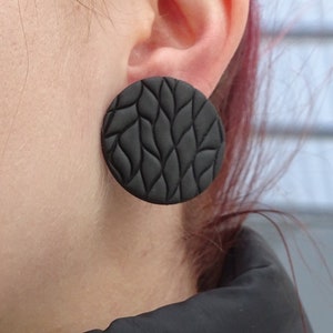 May include: A pair of black circular earrings with a textured, woven design.