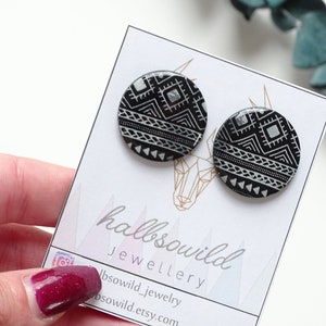 May include: A pair of black and silver geometric patterned stud earrings. The earrings are round and have a silver geometric pattern on a black background.