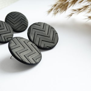 Op de afbeelding: Drie zwarte ronde oorbellen met een geometrisch zigzagpatroon.