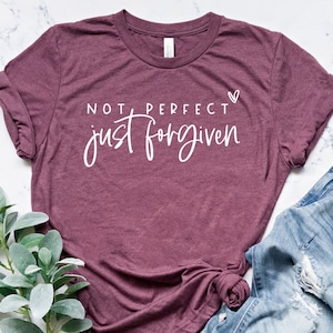 May include: A maroon t-shirt with the text "NOT PERFECT just forgiven" in white lettering with a small heart symbol.