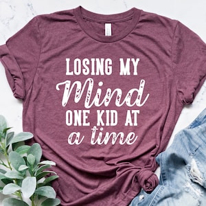 May include: A maroon t-shirt with the text "Losing my mind one kid at a time" in white.