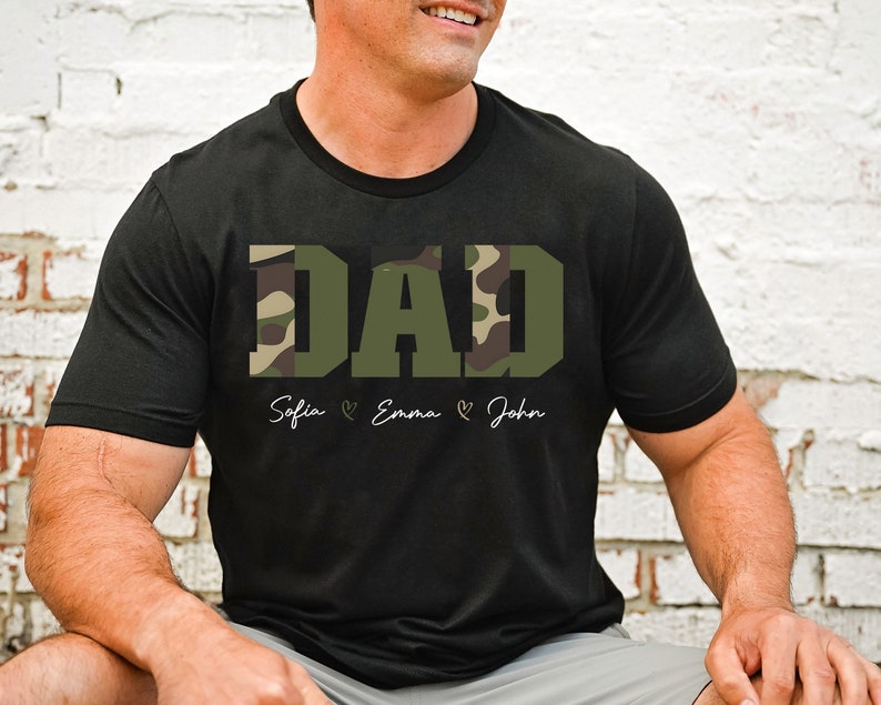 May include: Black t-shirt with a camouflage print "DAD" design. The shirt has the names "Sofia", "Emma", and "John" written below the design.