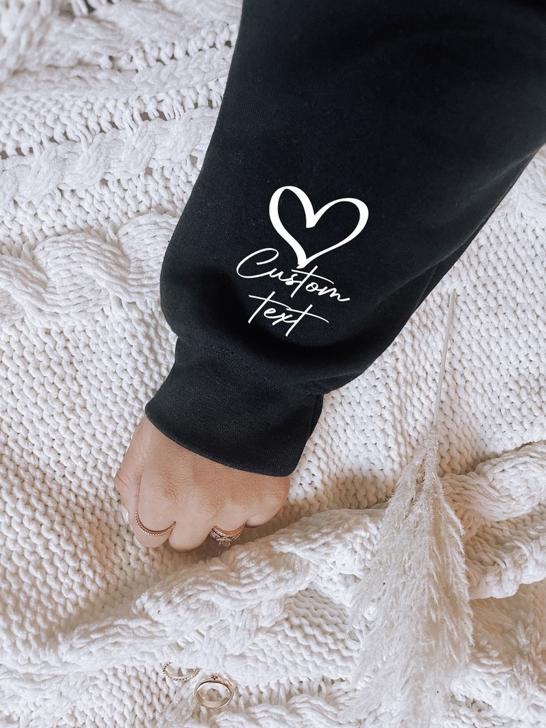 May include: Black sweatshirt with a white heart and the text "Custom Text" on the sleeve.