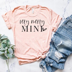 May include: A peach-colored t-shirt with the text "very merry mini" in black lettering with a small heart.
