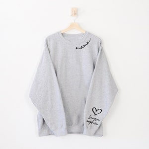 May include: Grey sweatshirt with the word "mama" written in cursive on the left shoulder and a heart with the words "laura sophia" on the right sleeve.