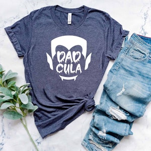 May include: A dark blue t-shirt with a white graphic of a vampire face and the text "Dadcula".
