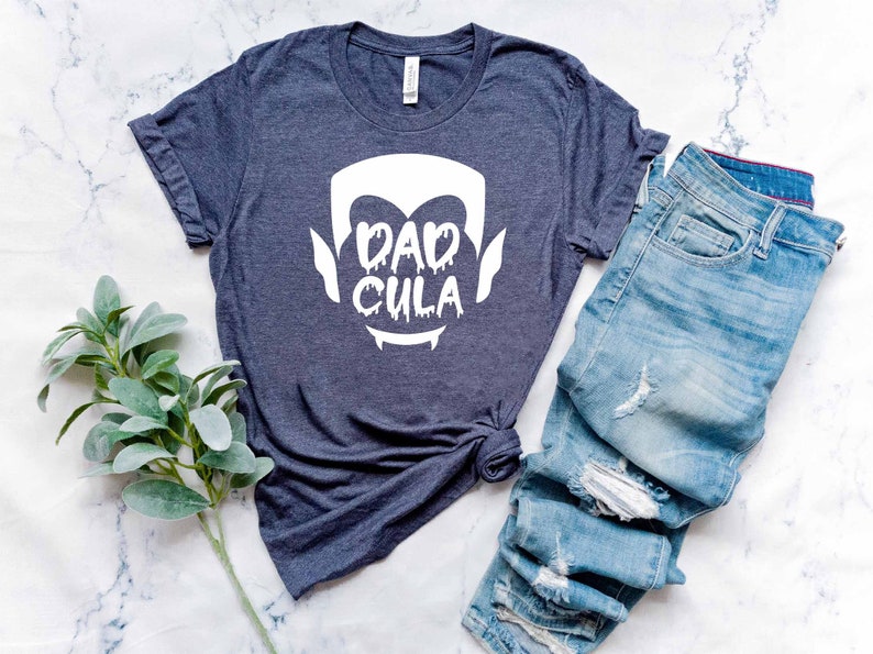 May include: A dark blue t-shirt with a white graphic of a vampire face and the text "Dadcula".