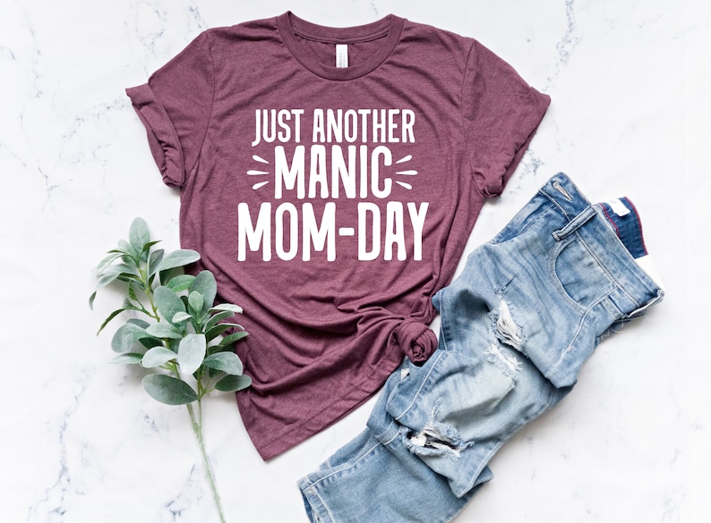 May include: A maroon t-shirt with the text "Just Another Manic Mom-Day" printed in white.