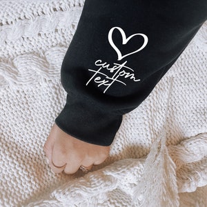 May include: Black sweatshirt with a white heart and the text "custom text" on the sleeve.