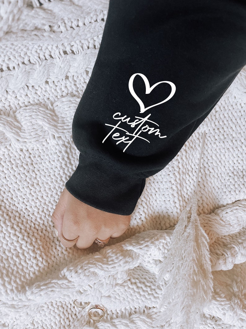 May include: Black sweatshirt with a white heart and the text "custom text" on the sleeve.