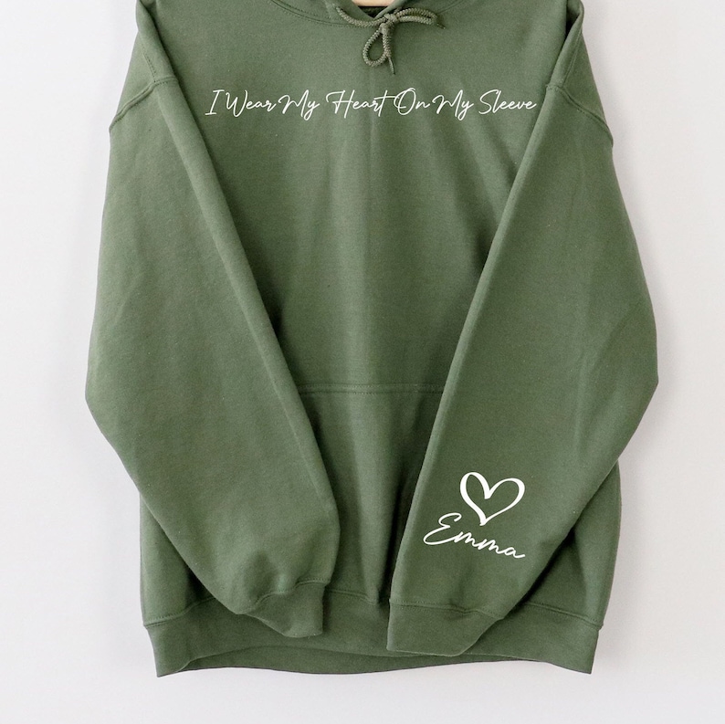 May include: A green hooded sweatshirt with the text "I Wear My Heart On My Sleeve" on the front and a white heart with the name "Emma" on the left sleeve.