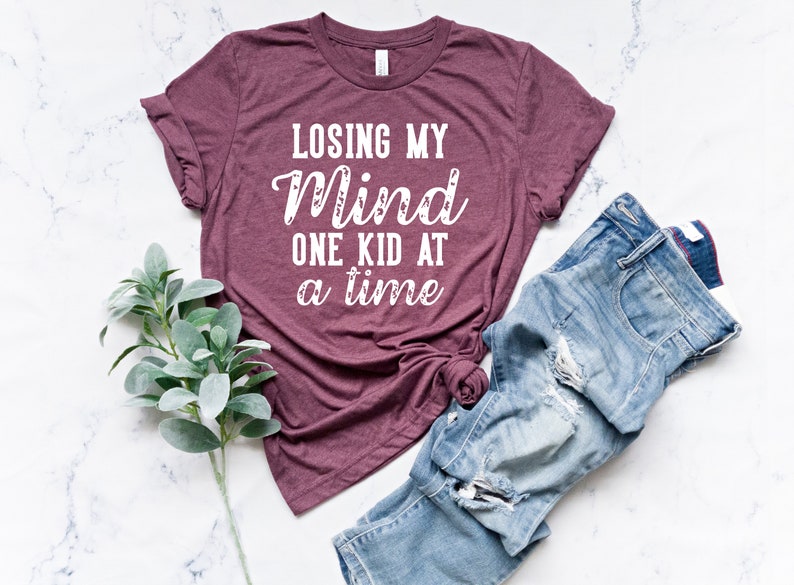 May include: A maroon t-shirt with the text "Losing my mind one kid at a time" in white.