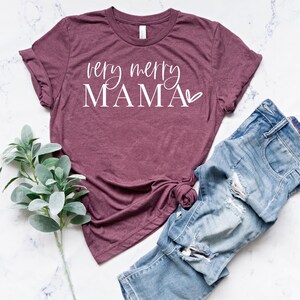 May include: A maroon t-shirt with the text "very merry MAMA" in white lettering with a small heart symbol.