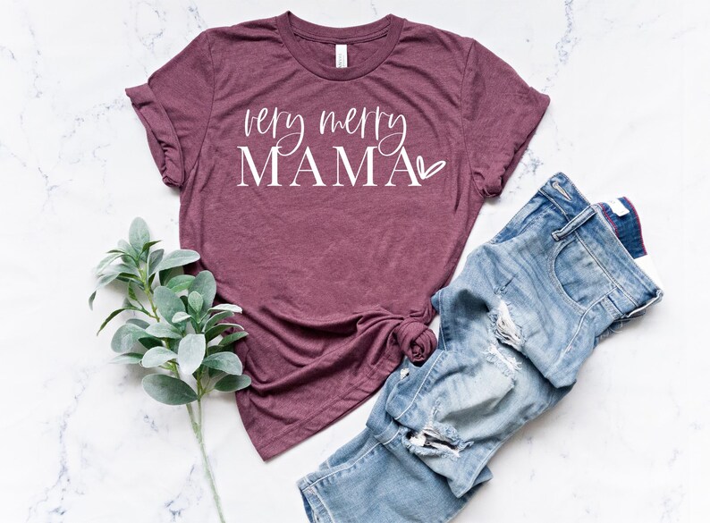 May include: A maroon t-shirt with the text "very merry MAMA" in white lettering with a small heart symbol.