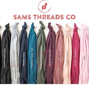May include: A display of folded t-shirts in various colors, including black, gray, navy, teal, and pink. The shirts are labeled with their color names, such as "Black" and "Heather Navy." The brand name "SAMS THREADS CO" is displayed at the top.