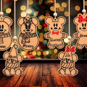 May include: Seven wooden Christmas ornaments shaped like Mickey Mouse characters. Each ornament has a different name on it: Anna, Henry, Lucas, Jenny, Alex, and Liz. The ornaments are hanging from a string and are against a blurred background of Christmas lights.