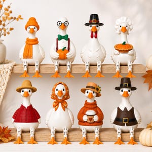 Puede incluir: Ocho figuras de gansos blancos dispuestas en dos estantes de madera. Los gansos llevan varios accesorios de temporada, como sombreros, bufandas, una pajarita y un pañuelo. Algunos sostienen objetos como una calabaza, un pastel o una taza de café.