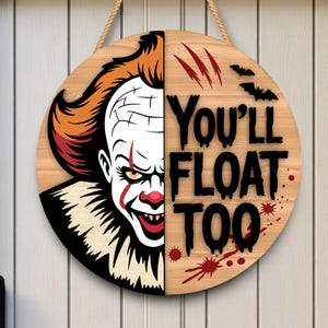 以下が含まれることがあります： オレンジ色の髪と赤いアクセントが特徴の不気味なピエロの顔が描かれた丸い木製の看板。「You'll Float Too」という文字が黒で書かれ、血しぶきとコウモリのシルエットが描かれています。吊り下げ用のロープが付いています。