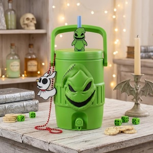 May include: A bright green cylindrical beverage dispenser featuring a molded Oogie Boogie face on the front, a handle, and a blue straw. A small white Zero character charm hangs from a red beaded chain attached to the side of the dispenser.