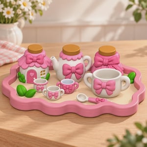 May include: A miniature tea set on a scalloped pink tray, featuring a house-shaped container, a teapot, a lidded jar, two small cups, a larger cup, and a spoon. The pieces are white with pink bows, pink roofs, and tan lids, accented by green leaves.