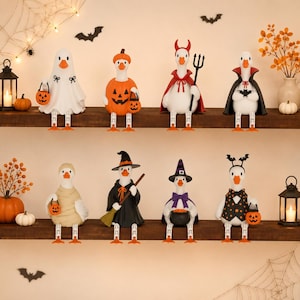 May include: A collection of eight white duck figurines dressed in various Halloween costumes, including a ghost, a pumpkin, a devil, a vampire, a mummy, a witch, a wizard, and a bat-themed outfit, all sitting on two wooden shelves.