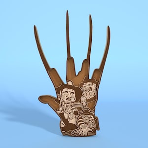 Op de afbeelding: Een houten handvormige sculptuur met lange, scherpe bladen, met gegraveerde afbeeldingen van een horrorfilmkarakter. De sculptuur is bruin met een lichtbruine gravure.