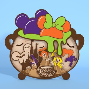 May include: Wooden Halloween decoration featuring a cauldron with Mickey Mouse ears, a green and orange bow, and the text "Hocus Pocus." The cauldron contains silhouettes of bats, a castle, and three witch characters. The color scheme includes brown, purple, orange, and green.