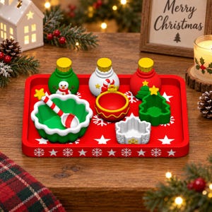 May include: A rectangular red serving tray decorated with white stars and snowflakes, holding three small round containers, a green scalloped bowl with a red and white striped spoon, a red ornament-shaped bowl, and a green tree-shaped bowl.